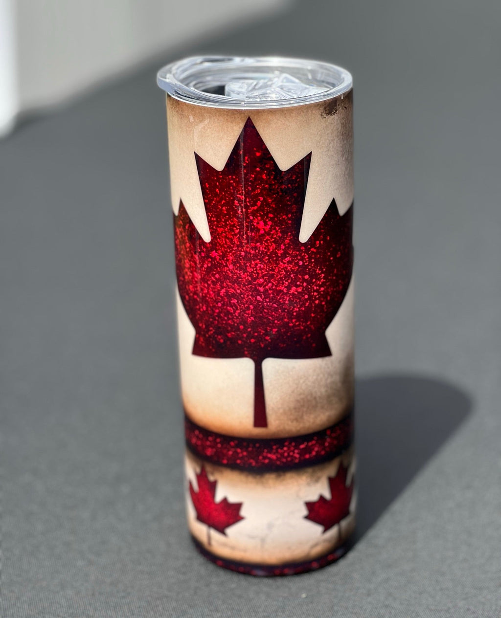 Tumbler with red maple leaf design on a gray surface
