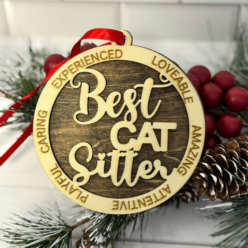 Decorative ornament with 'Best Cat Sitter' text on a wooden background with pine cones and berries.